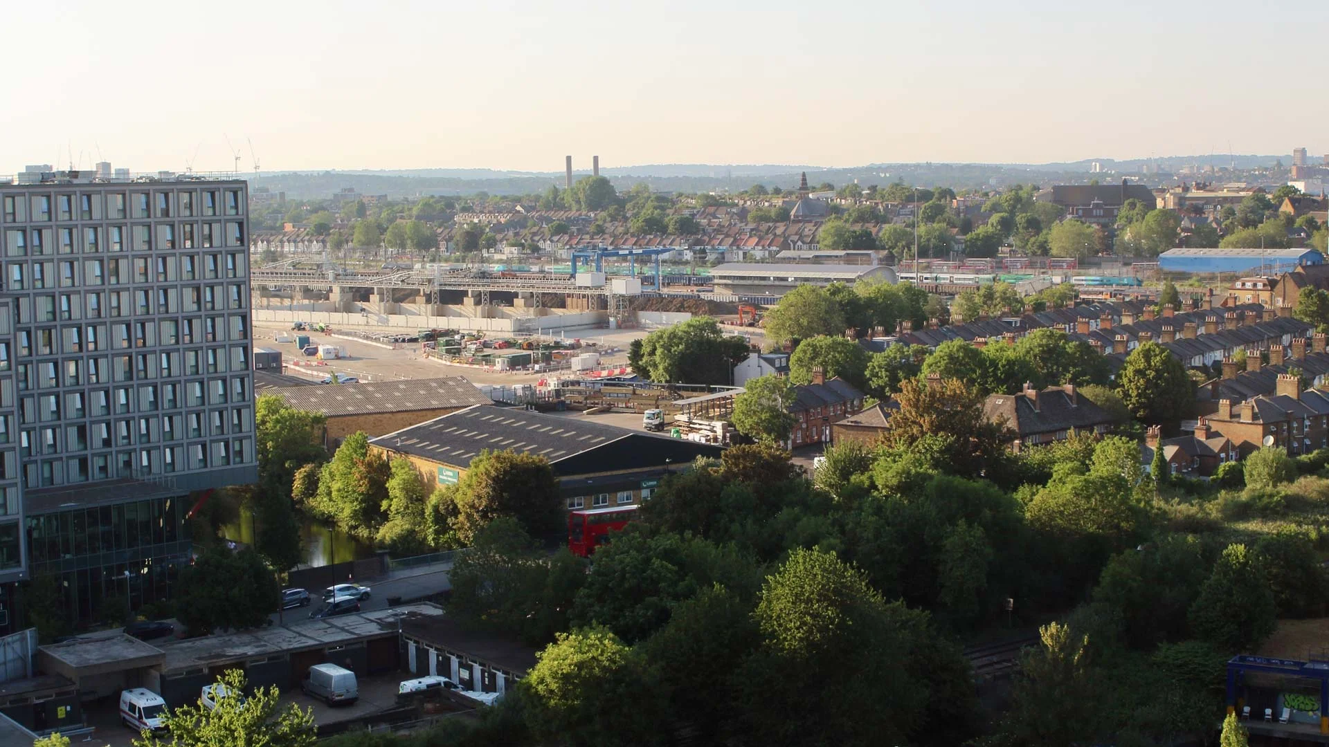 High-rise aerial view overlooking urban London residential neighborhoods, lush green trees, roads, and active construction development zones