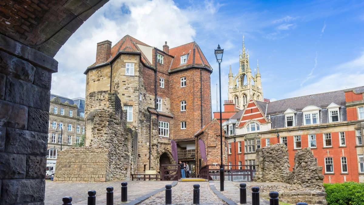 Historic stone castle gateway and medieval architecture framed by an arched stone entryway under a bright blue sky