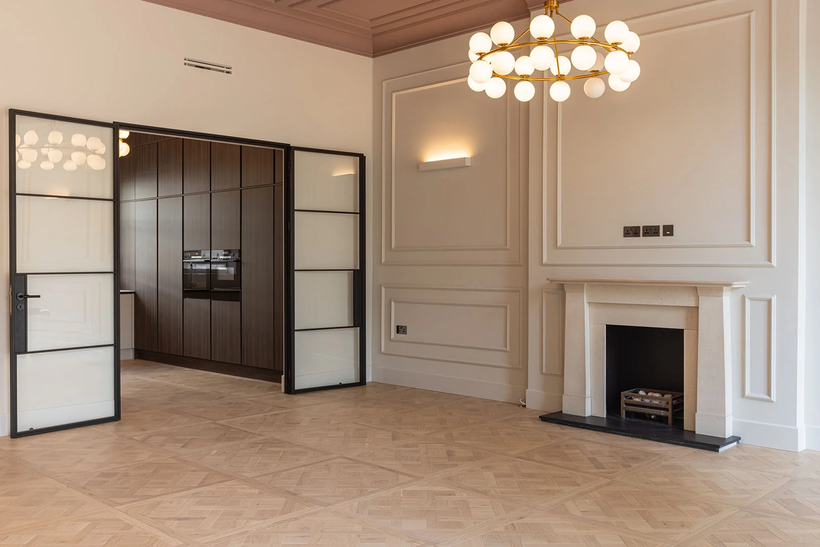 Elegant living room featuring bespoke wall panelling, a stone fireplace, parquet flooring, and glazed doors leading to a custom kitchen in a London home renovation.