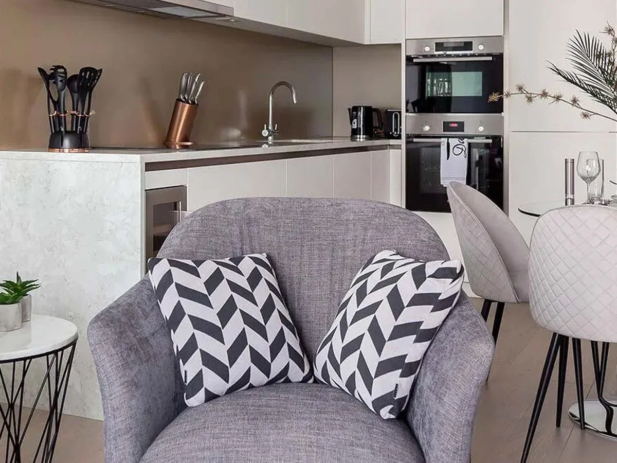 Modern furnished apartment living room with grey armchair and open-plan kitchen