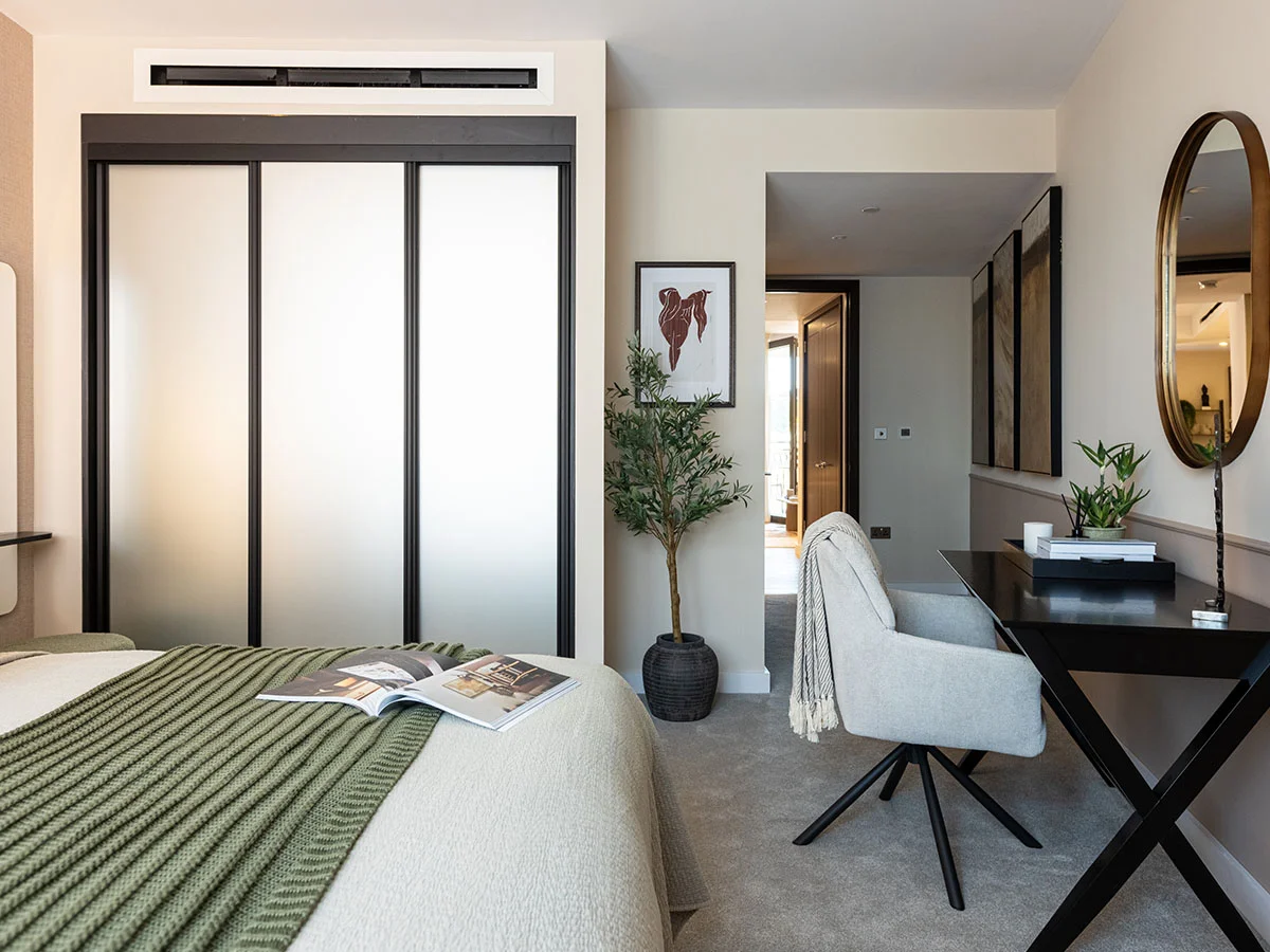 Modern bedroom with integrated study area, mirrored wardrobe, and contemporary furnishings at West End Gate, London.