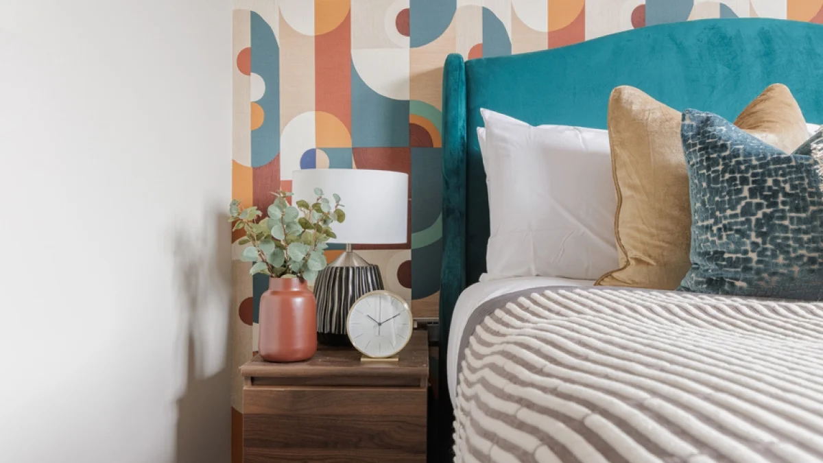 Airbnb bedroom featuring a teal upholstered headboard, layered cushions and coordinated bedside accessories for a comfortable guest stay.