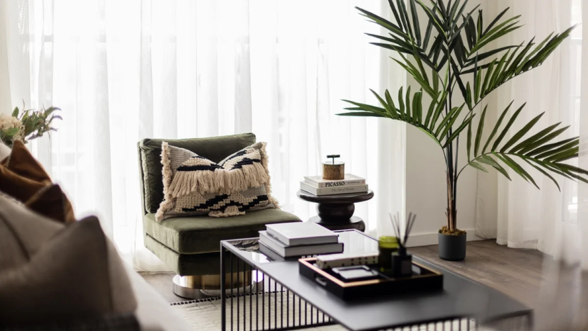 Airbnb living room with a green accent chair, indoor palm and contemporary coffee table, showcasing thoughtful furnishing for guest comfort.