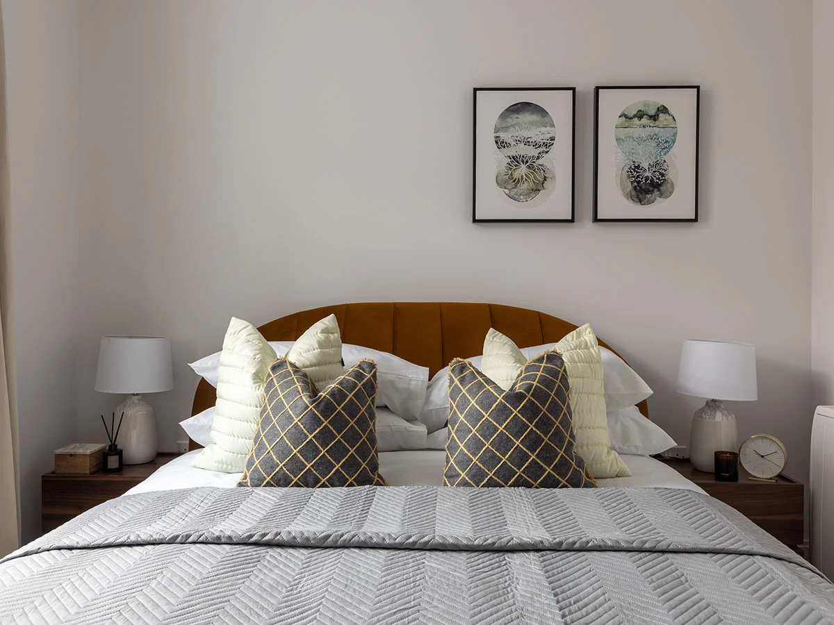 Modern staged bedroom at Horlicks Quarter featuring a curved upholstered headboard, layered cushions, bedside tables and contemporary wall art.