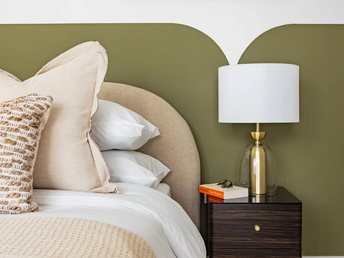 Close-up of a boutique bedroom setup styled by InStyle Direct at Regents View, featuring a painted scalloped olive green wall feature, an arched fabric headboard, and a brass-and-glass bedside table lamp