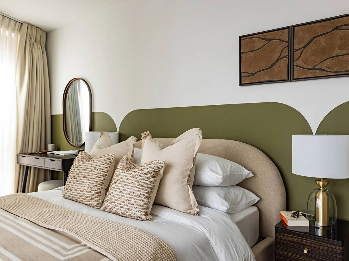 A boutique hotel-style bedroom staged by InStyle Direct featuring a unique scalloped olive green wall feature, textured beige throw cushions, a dark wood nightstand, and a contemporary gold globe table lamp