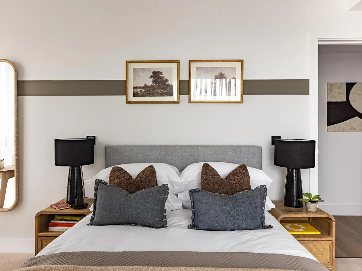 A contemporary bedroom interior package styled by InStyle Direct at Regents View, showing a grey fabric headboard, a horizontal brown wall stripe, symmetrical black ceramic bedside lamps, and curated timber nightstands