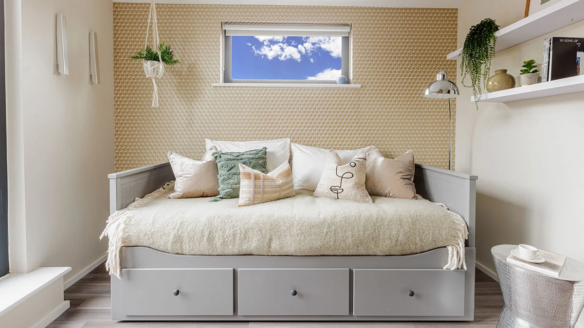 A contemporary multi-functional guest bedroom styled by InStyle Direct featuring a grey wooden daybed with pull-out drawers, textured throw pillows, a macramé hanging planter, and subtle geometric patterned wallpaper in Islington