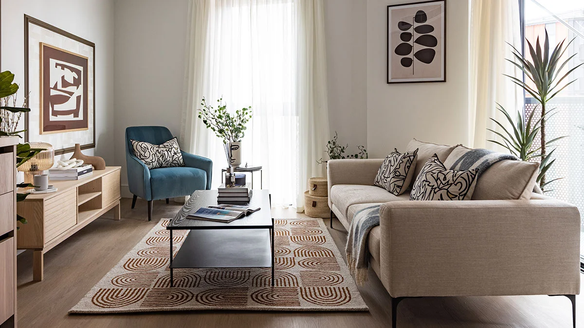 Stylish living room interior featuring a beige sofa, a teal accent armchair, a black coffee table over a geometric patterned rug, and abstract wall artwork