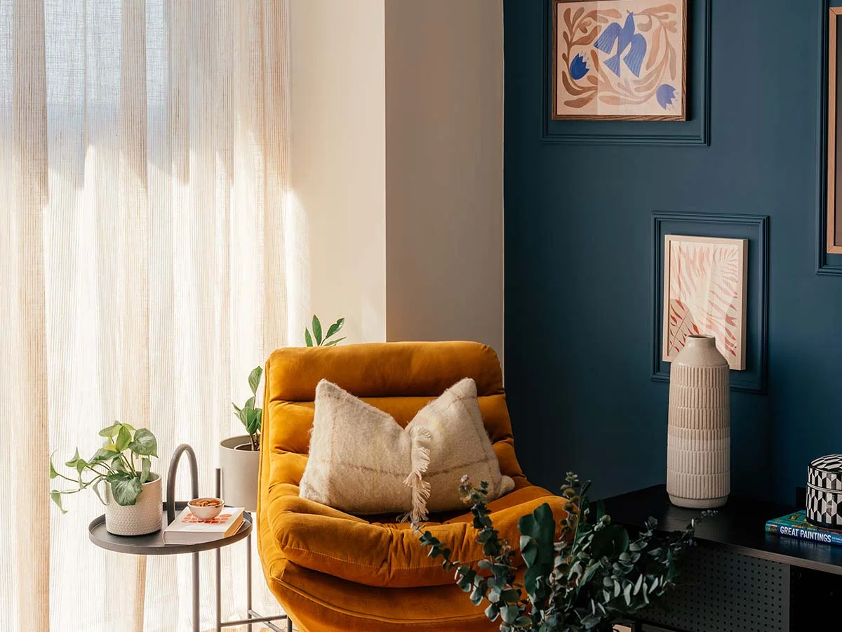 A contemporary living space detailed by InStyle Direct with deep teal panelled walls, small abstract art frames, a mustard-yellow velvet swivel armchair, and a minimalist black side table