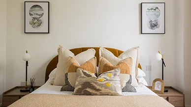 A designer bedroom interior styled by InStyle Direct at PLATFORM_ Glasgow, showcasing a scalloped ochre headboard, layered patterned cushions in earth tones, and minimalist black bedside lamps