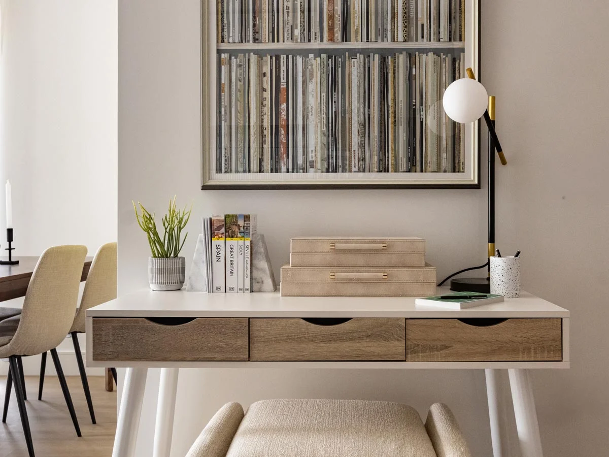 Modern home office desk setup featuring a white and wood-grain table, stylish storage boxes, a black modern desk lamp, and a large record shelf artwork hanging above