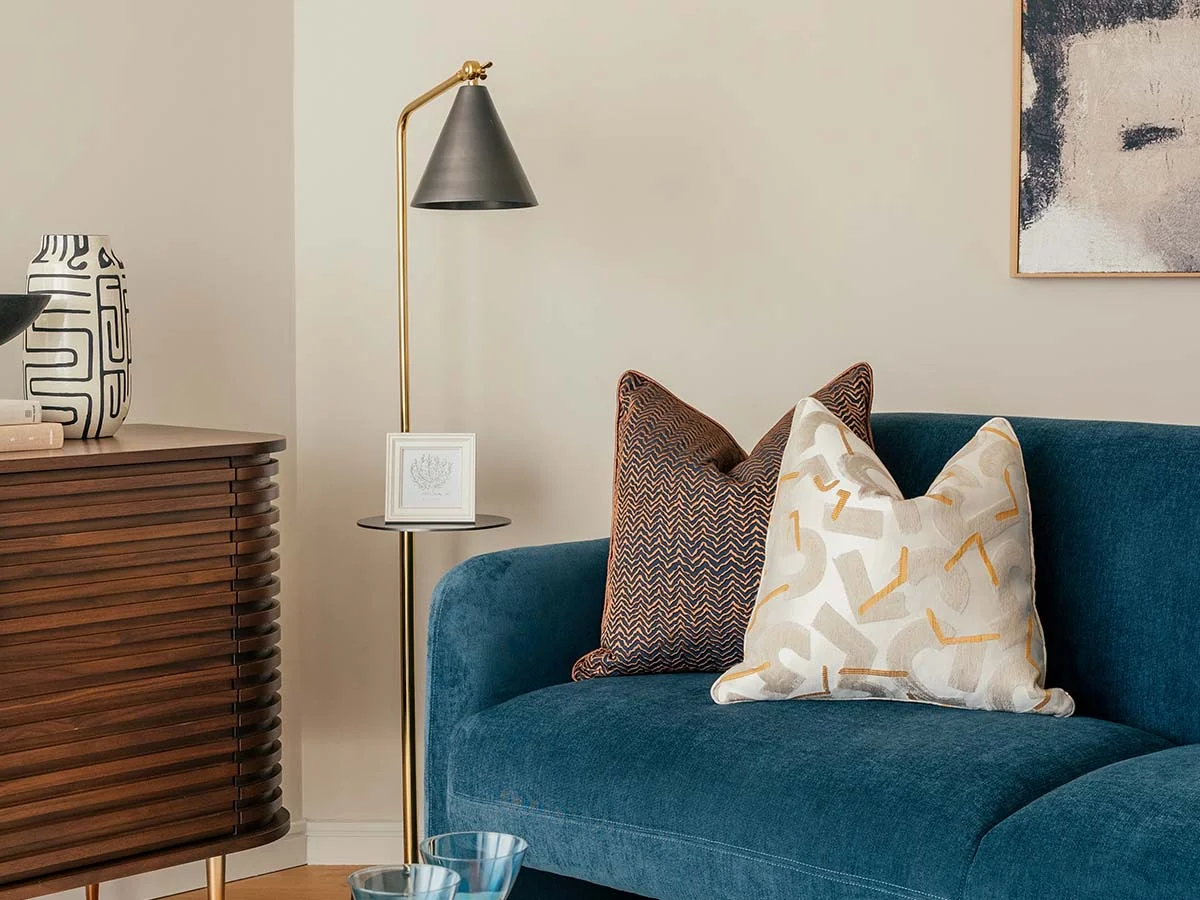 A luxury living room vignette styled by InStyle Direct featuring a deep teal velvet sofa with abstract chevron scatter cushions, a fluted dark wood sideboard, and a sleek matte black floor lamp in Battersea