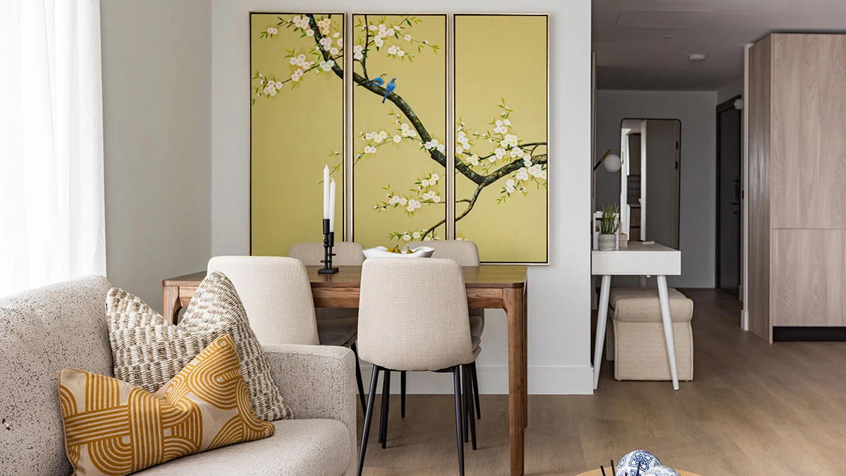 Elegant open-plan dining space featuring a wooden table with upholstered chairs beneath a triptych botanical art canvas and a neutral textured sofa in the foreground