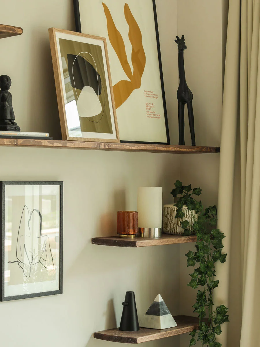 Warm open timber wall shelving styled by InStyle Direct at Sugar House Island, Stratford, displaying framed minimalist art prints, a sculpted giraffe figurine, ambient candles, and trailing greenery