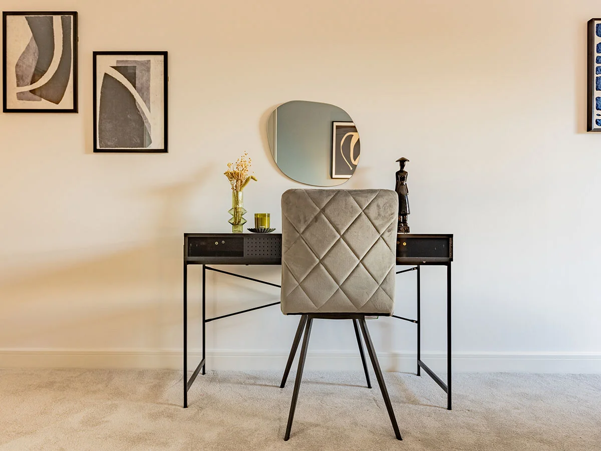 Modern home office with a black desk, upholstered chair, decorative mirror and contemporary artwork in a furnished London apartment.