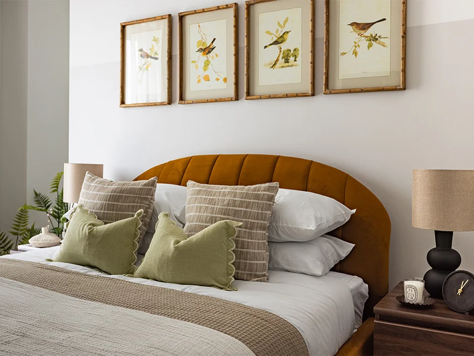 Elegant bedroom with curved mustard headboard, layered cushions, and framed bird artwork