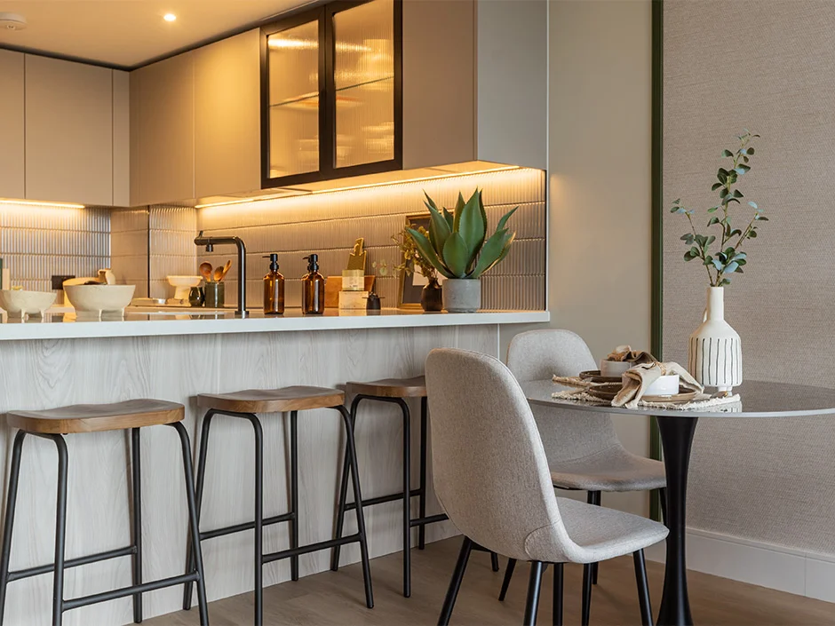 Modern kitchen with breakfast bar seating, ambient lighting, and neutral dining setup in Regents View show home
