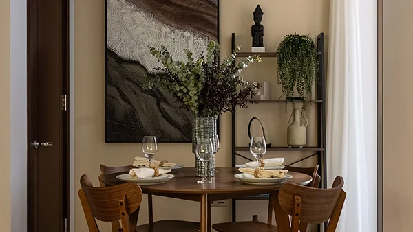 A round walnut dining table setting styled by InStyle Direct at West End Gate, featuring mid-century wooden chairs, fine stemware, a tall eucalyptus vase, and a open shelving unit in Paddington