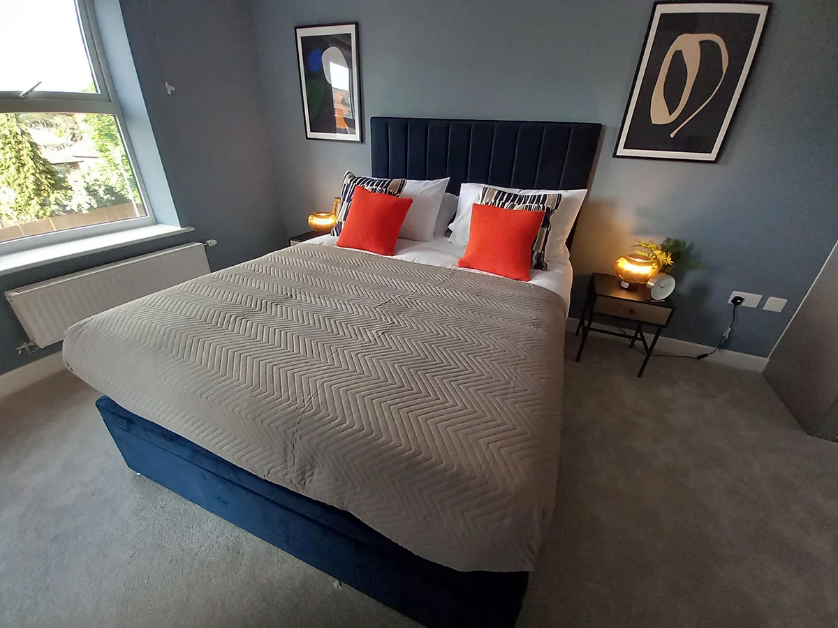 Stylish second bedroom featuring a blue upholstered bed, feature wall, bedside tables and contemporary artwork in a London apartment.
